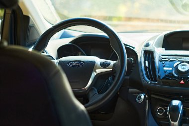 Sıcak güneş ışığında direksiyon, gösterge paneli ve merkez konsolu gösteren Ford 'un iç kısmının yakın çekimi. Araçların modern tasarımı ve özelliklerini vurgular.