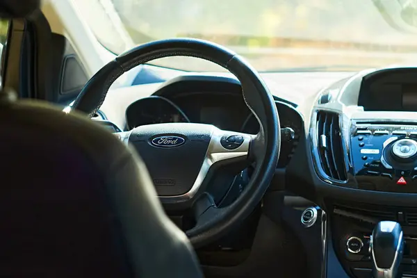 Sıcak güneş ışığında direksiyon, gösterge paneli ve merkez konsolu gösteren Ford 'un iç kısmının yakın çekimi. Araçların modern tasarımı ve özelliklerini vurgular.
