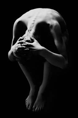 Kafatası şeklinde kıvrılmış güçlü siyah beyaz bir insan figürü. Işıklandırma derin gölgeler yaratıyor, çıplak omurgayı ve saf duyguları vurguluyor..