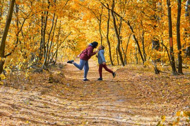 Sonbahar giysileri içinde bir kadın ve oğlu canlı bir sonbahar yeşilliği olan bir ormanda neşe içinde poz veriyorlar. Ağaçlar altın ve turuncu yapraklarla süslenir, bu da güzel bir sonbahar sahnesi yaratır.