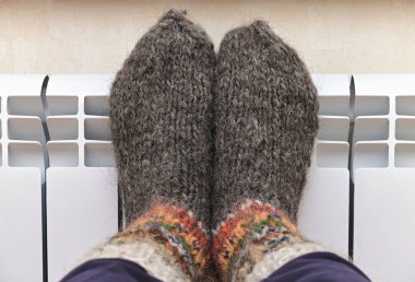 Sıcak bir radyatörde dinlenen yün çoraplı ayaklar. Soğuk havada rahatlatıcı, sıcak bir atmosfer, ısınarak enerji tasarrufunu teşvik ediyor..