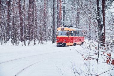 A single vintage red and yellow tram travels through a snow-covered forest in the midst of a heavy snowfall. The peaceful winter landscape enhances the charm of this retro mode of transportation. clipart