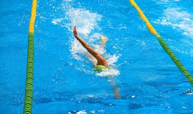 Mavi yüzme havuzu şeritleri, sporun sembolü. Yeşil şapkalı bir yüzücü, parlak mavi bir havuzda bedavaya yüzüyor, su sıçratıyor..