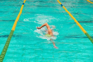 Yüzücü kapalı bir havuzda hareketli şerit işaretleri ve berrak mavi suyla serbest stil inme hareketi yapıyor. Hareketi yakalar ve rekabetçi yüzmeye odaklanır.