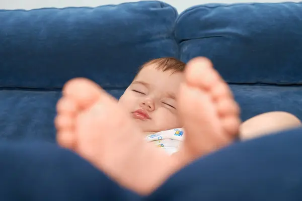 Huzurlu bir bebek, ön plandaki küçük ayaklarıyla yumuşak, mavi bir kanepede uyur, rahatlatıcı bir rahatlama ve masumiyet anı yaratır..