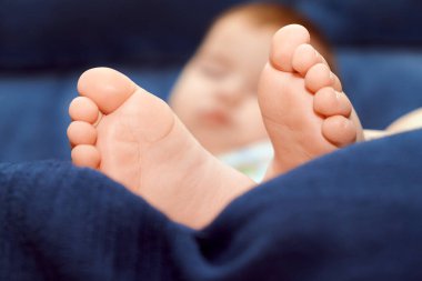 Huzurlu bir bebek, ön plandaki küçük ayaklarıyla yumuşak, mavi bir kanepede uyur, rahatlatıcı bir rahatlama ve masumiyet anı yaratır..