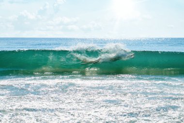 Genç bir adam çarpan bir turkuaz dalgaya dalıyor, tamamen suya dalmış. Güneş ışığı okyanus yüzeyinde parıldıyor, dinamik ve ferahlatıcı bir macera ve yaz eğlencesi sahnesi yaratıyor..