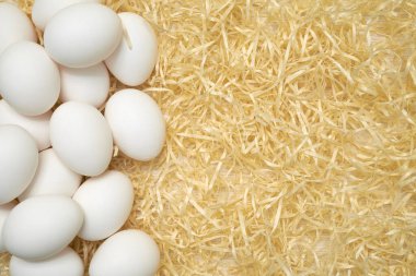 Doğal saman arka planında taze beyaz yumurtalar. Sol taraftaki organik çiftlik yumurtaları sağ tarafta boş alan bırakıyor. Sıcak, yumuşak renk paleti olan minimalist kırsal kavram.