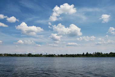 Mavi gökyüzü ve tüylü beyaz bulutlarla Kakhovka Barajı 'nın manzarası. Durgun su yaz gökyüzünü yansıtarak Nikopol, Ukrayna yakınlarında barışçıl bir doğal manzara yaratır..