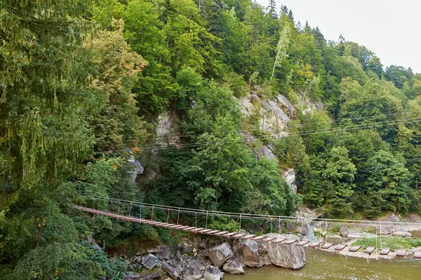 Bir köy asma köprüsü yemyeşil bir ormanda bir dağ nehrinden geçer. Tahta kalaslar ve kablolar sarp kayalıklar ve yoğun yeşilliklerle çevrili manzaralı ama maceralı bir yol oluşturuyor..