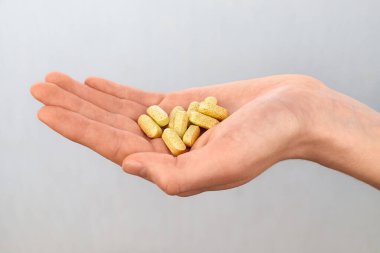 Beyaz plastik bir şişeden sarı vitamin hapları döken yakın plan bir el. Sağlık, beslenme takviyeleri ve ilaç konsepti.