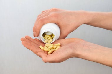 Beyaz plastik bir şişeden sarı vitamin hapları döken yakın plan bir el. Sağlık, beslenme takviyeleri ve ilaç konsepti.