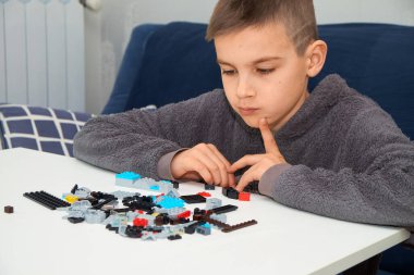 Masada renkli plastik tuğlalar birleştiren odaklanmış genç bir çocuk. Yaratıcı bir yapıyla ilgileniyor, problem çözme becerileri ve hayal gücü geliştiriyor. Evde eğitici oyun.