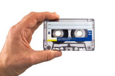 İnsan eli, beyaz arka planda izole edilmiş klasik bir ses kaseti tutuyor. Analog müzik nostaljik kavramı, retro medya ve 80-90 'ların kültürü.