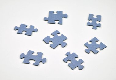 Beyaz bir yüzeye dağılmış birkaç mavi yapboz parçası. Bireysel şekillere, dokulara ve negatif uzaya odaklı basit bir kompozisyon. Eksik parça veya problem çözme kavramı.