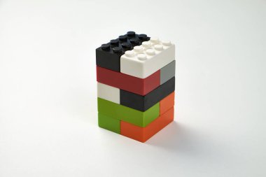 Beyaz arka planda dikey olarak dizilmiş renkli plastik oyuncak yapı taşları düzgün bir dikdörtgen kule oluşturuyor. Modern ve minimalist tasarım.