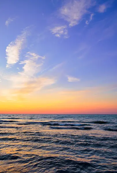 Sakin bir denizin üzerinde, hafif dalgalar ve canlı bir gökyüzü olan renkli bir gün batımı. Huzurlu okyanus manzarası seyahat, rahatlama ya da doğa temaları için mükemmeldir..