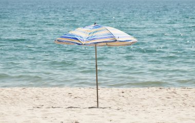Çizgili plaj şemsiyesi beyaz arka planda izole bir şekilde beyaz kumun üzerinde duruyor. Şemsiye gölge ve yaz havası sağlıyor..