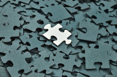 Tek bir beyaz yapboz parçası koyu yeşil parçalar arasında duruyor. Eşsizliğin, çözümün ve bireyselliğin sembolü. Makro konsept resmini kapat.