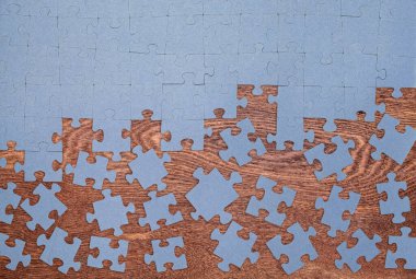 Ahşap arka planda bitmemiş mavi bulmaca. Tamamlanmamış yapboz parçaları dağılmış, problem çözmeyi, meydan okumayı, yaratıcılığı ve süreci sembolize ediyor.