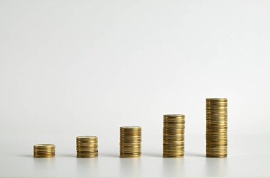 Beyaz arka planda yükselen altın para yığınları, mali büyüme, yatırım ve tasarrufu sembolize ediyor.