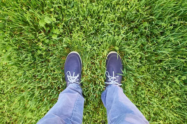 Mavi süet ayakkabılı ve sıradan mavi pantolonlu yemyeşil çimlerin üzerinde duran birinin yukarıdan görünüşü. Canlı renklere ve doğal dokulara sahip taze bahar ya da yaz konsepti.