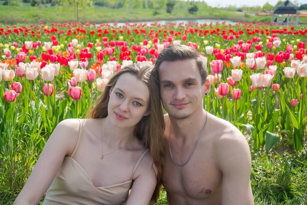 Genç Güzel Gülümseyen Bir Çift Renkli Lalelerin Arka Planında Oturuyor — Stok fotoğraf