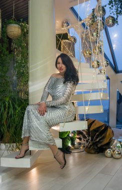 Güzel bir kadın parlak gümüş bir elbise giyiyor. Parlak toplarla Noel süslemeleri oturuyor..