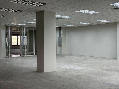 Geniş mobilyasız ofis, tavan lambaları, beton zemin ve cam giriş, emlak ve ticari kiralama kavramları için ideal..