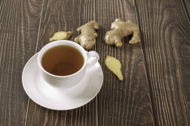 Bir fincan zencefilli çay, kök ve ahşap arka planda dilimler..