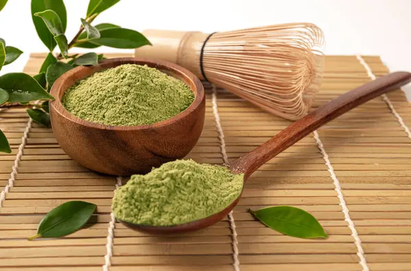 matcha green tea powder with whisk, spoon and bowl with green tea leaves on table, close view