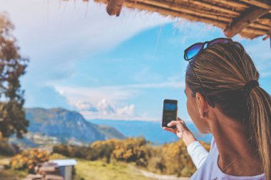 Kadın, dağ başında kulübede gün batımının keyfini çıkarırken kadın, denizin üstünde güneşin doğuşunu, tepeleri fotoğraflıyor.