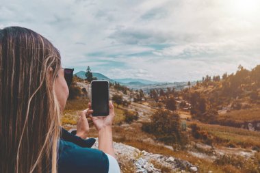 Back view portrait of a woman taking photo of a landscape with a smart phone in springtime