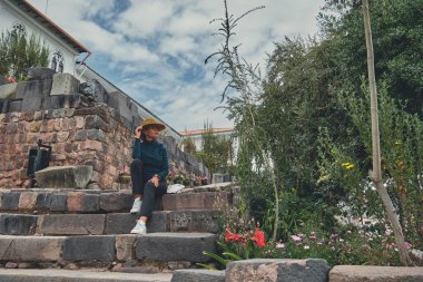 Cusco, Peru 'daki Qorikancha iç bahçelerini keşfeden şık bir turist. Tarihle doğanın büyüleyici bir karışımı..