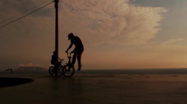 BMX motoru havada yüksekte. Genç adam gün batımında BMX bisikleti üzerinde rampa atlayışı yapıyor.