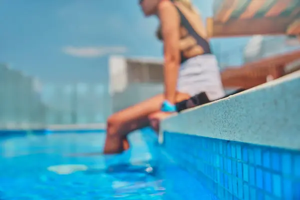 Young woman relaxing at side of pool, low section