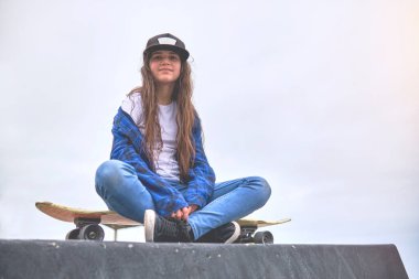 Kaykay parkında kaykay sürerken eğlenen çekici şehir kızı, elinde kaykayıyla gülümseyen genç bayan kaykaycının portresi. Eğlence Faaliyeti Konsepti