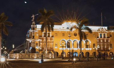 Önünde çeşme olan büyük bir bina. Bina gece aydınlanıyor.