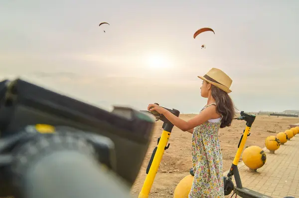 女の子がビーチでスクーターに乗っている 空は曇り 太陽は沈んでいる ストック画像
