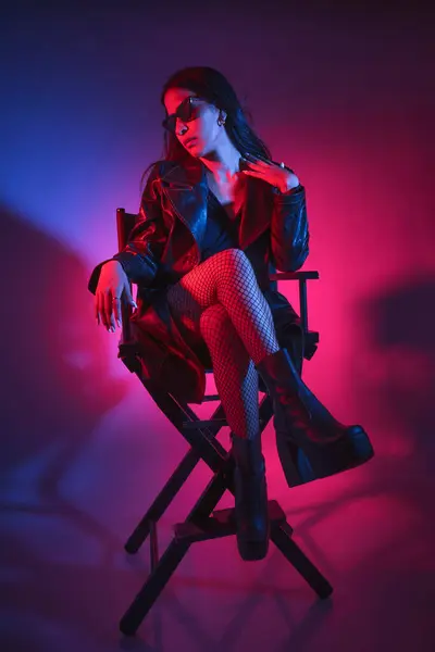 女性が黒いジャケットと黒いストッキングの椅子に座っています 彼女は黒いブラジャーを着て 髪を引っ張った イメージは暗くてムーディーな雰囲気を持っています ロイヤリティフリーのストック画像