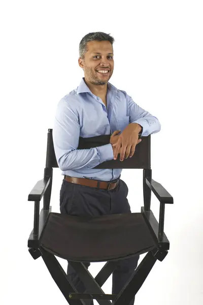 男が椅子の前に立っている 彼は微笑んで青いシャツを着ている 椅子は黒く 茶色のクッションを持っています ストック写真