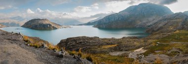 Rıhtımı ve birkaç teknesi olan bir göl. Gökyüzü mavi ve dağlar arka planda.