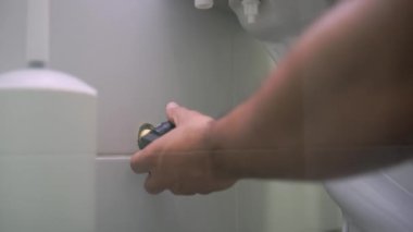Birisi ingiliz anahtarıyla tuvaleti tamir ediyor. Beyaz tenli bir tamirci elleri evin içindeki bir banyoda gevşek bir tuvaleti oynatır.