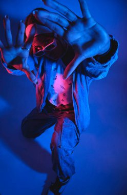 Mavi ceketli ve kot pantolonlu bir adam elleri havada fotoğraf için poz veriyor. Fotoğraf mavi ve mor renkte, serin ve keskin bir hava veriyor.