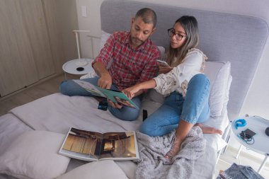 Bir adam ve bir kadın bir yatakta oturmuş, bir kitaba bakıyorlar. Sahne rahat ve samimi, çünkü çift birlikte vakit geçiriyor.