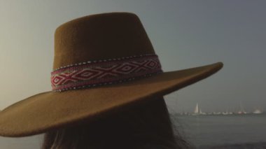 Kırmızı ve beyaz çizgili kahverengi şapkalı bir kadın. Şapka kafasında ve kameraya bakıyor.