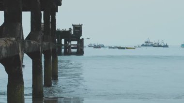 Suyun içinde bir sürü tekne olan bir rıhtım. Teknelerin boyutları ve renkleri farklı. Su sakin ve gökyüzü bulutlu.