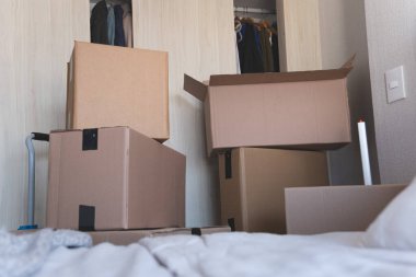 Üst üste yığılmış bir sürü kutunun olduğu bir oda. Kutular kahverengi ve nakliye şirketinden gibi görünüyor. Oda boş ve kutular bir köşeye yığılmış.