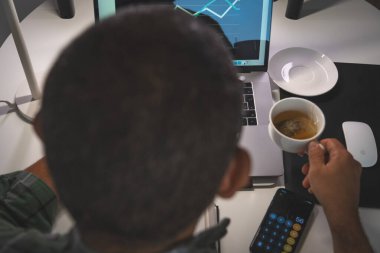 Bir adam elinde dizüstü bilgisayar ve bir fincan kahveyle masada oturuyor. Elinde bir cep telefonu ve bir fare var. Verimlilik ve odaklanma kavramı