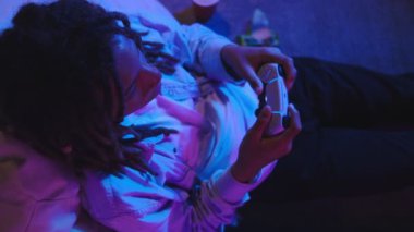 Oturma odasındaki kanepede oturan mutlu genç latin çift evde video oyunları oynayarak eğleniyorlar. Konsept Oyun Akımı
